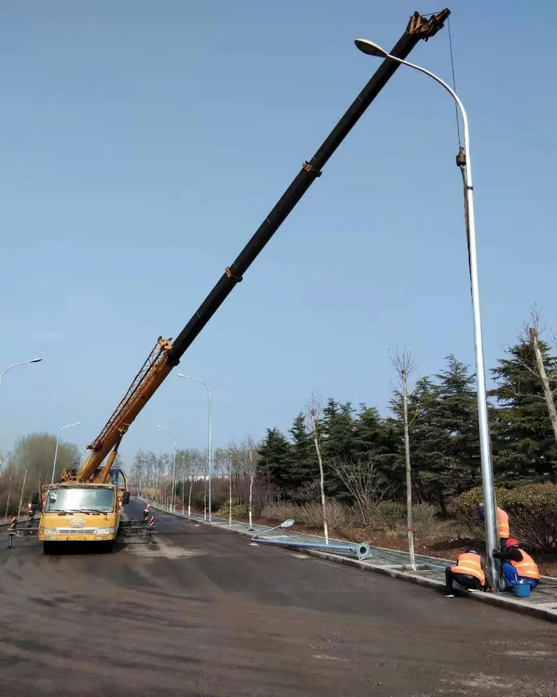 吊车配合施工人员在新建道路旁安装单臂路灯